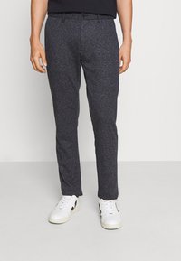 Pantaloni grigio scuro, con texture, a vestibilità slim e vita elastica, abbinati a sneakers bianche con dettagli neri.