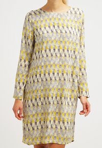 Robe à manches longues en tissu léger avec un motif géométrique jaune et violet sur fond neutre. Encolure ronde.