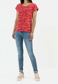 Top rosa de manga corta con un patrón vibrante, combinado con jeans ajustados de color azul claro y zapatillas rosas con suelas blancas.