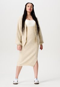 Beige geribbelde sweater cardigan met grote knopen, gecombineerd met een bijpassende geribbelde midi-rok met een zijsplit, gedragen met witte sneakers.