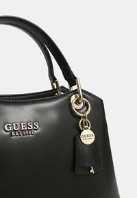 Borsa a mano in pelle nera con finiture dorate lucide, dotata di un portachiavi e logo impresso. Texture liscia e forma strutturata con doppi manici.