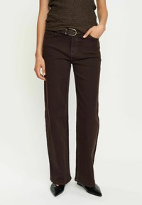 Jeans larghi marroni con parte frontale piatta, passanti per la cintura e cuciture a contrasto. Il tessuto ha una trama liscia e presenta un classico design a cinque tasche.