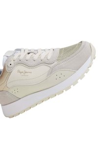 Beige sneaker with light green accents, made from textured synthetic material and suede. Features traditional lacing and a white sole.