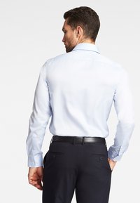 Camicia da dress leggera blu con maniche lunghe e polsini a bottone, abbinata a pantaloni da dress neri con due tasche posteriori e una cintura nera.