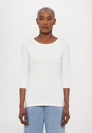 Maglietta bianca a maniche lunghe con scollatura rotonda, realizzata in tessuto leggero. Abbinata a pantaloni in denim azzurri. Design semplice e aderente.