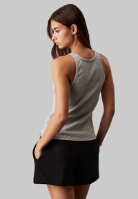 Top in grigio senza maniche realizzato in tessuto morbido, con scollatura rotonda, silhouette aderente e spacchi laterali, abbinato a pantaloni corti neri.