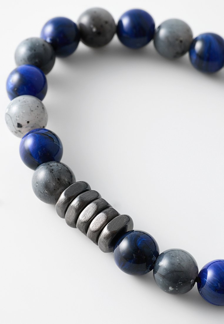 Bracciale di perline con pietre rotonde blu e grigie e uno spacatore in metallo texturizzato, che mostra una finitura liscia e lucida con tonalità variabili.