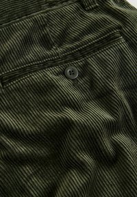 Olive green corduroy fabric with prominent vertical ribbing, featuring a four-button closure on the back pocket for secure storage.