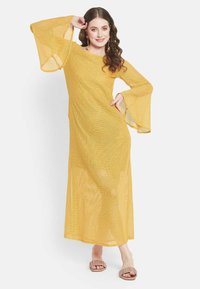 Gelbes, langes, transparentes Kleid mit Glockenärmeln, gefertigt aus einem leichten, strukturierten Stoff. Das Model trägt neutrale Sandalen, die Haare sind in lockeren Locken gestylt.
