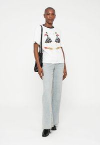 Vit bomullst-shirt med svarta prickiga illustrationer av två figurer, ihop med ljusblå vida jeans och svarta anklar stövlar.