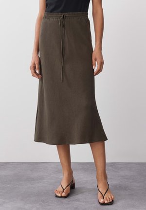 Jupe midi vert olive avec une taille à cordon, présentant une forme légèrement évasée et une fente sur le côté. Fabriquée en tissu doux et texturé.