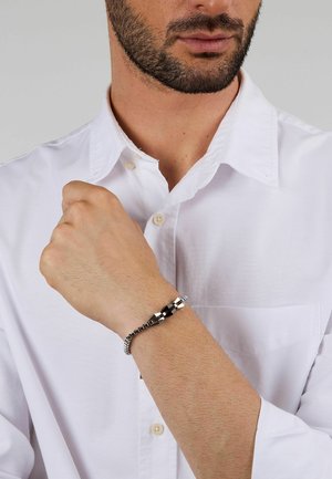 Bracciale in tonalità argento con accenti esagonali, segmenti neri alternati a quelli lucidi e un design a catena flessibile, indossato su un polso.