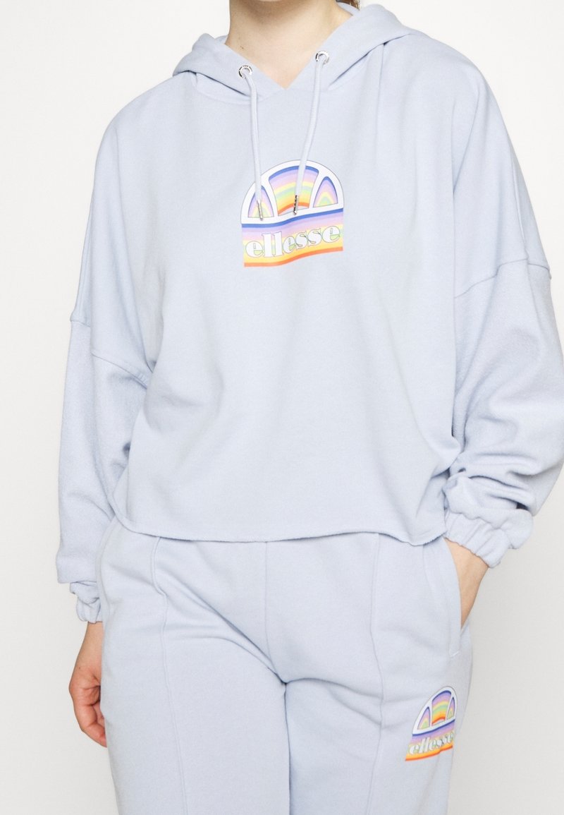 Felpa leggera blu con una vestibilità ampia, caratterizzata da una grafica arcobaleno e un logo. Tessuto morbido con cordino regolabile sul cappuccio.