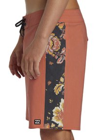 Shorts de bain pour hommes en corail avec une bande d'accent florale noire. Dotés d'une taille à cordon de serrage et d'une patch logo plat en bas.