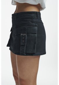 Jupe mini en denim noir à taille haute, avec une poche latérale à bouton-pression et un ourlet brut pour une finition texturée.