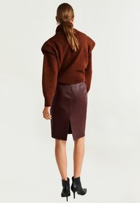 Ruskea neulottu paita korkealla kauluksella, yhdistetty viininpunaisen nahkaseelikön kanssa, jossa on takana halkio, sekä mustat nilkkurit korolla.