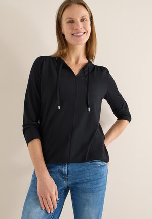 Černá mikina s kapucí, výstřihem do V, tříčtvrtečními rukávy a šňůrkami, v kombinaci s modrými úzkými džínami. Hladká tkanina a pohodlný střih.