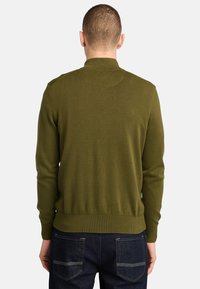 Olivengrüner Strickpullover mit Rundhalsausschnitt. Verfügt über gerippte Bündchen und Saum, hat eine glatte Textur und wird mit dunkelblauen Jeans kombiniert.