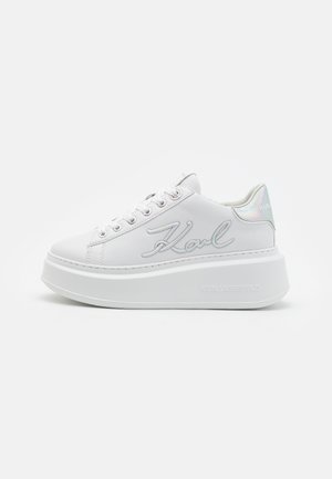 Sneaker bianco con tomaia in materiale sintetico liscio, punta rotonda, occhielli metallici e suola piatta spessa. Presenta un tallone riflettente e lettere con marchio.