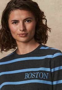 Grå langærmet skjorte med lyseblå striber og "BOSTON" broderet i blå. Blødt stof og rund halsudskæring.