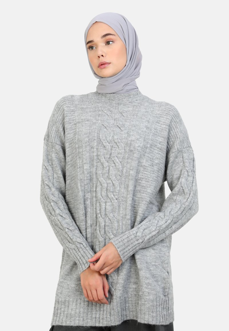 Grå strikket sweater med kabeldesign, løs pasform, ribbede manchetter og kant. Kombineret med et lysegråt hijab for et koordineret look.