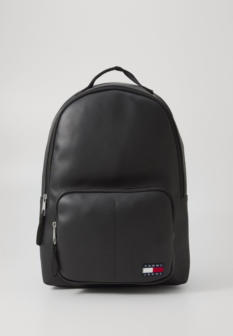Black backpack made of smooth synthetic material, featuring a front zippered pocket, curved shape, and a logo patch on the lower right side.