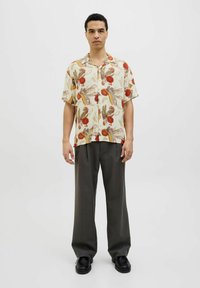 Cămașă cu mânecă scurtă în nuanță de crem, cu un model floral în roșu, maro și verde. Pantaloni gri, cu picioare largi, și pantofi negri completează ținuta.