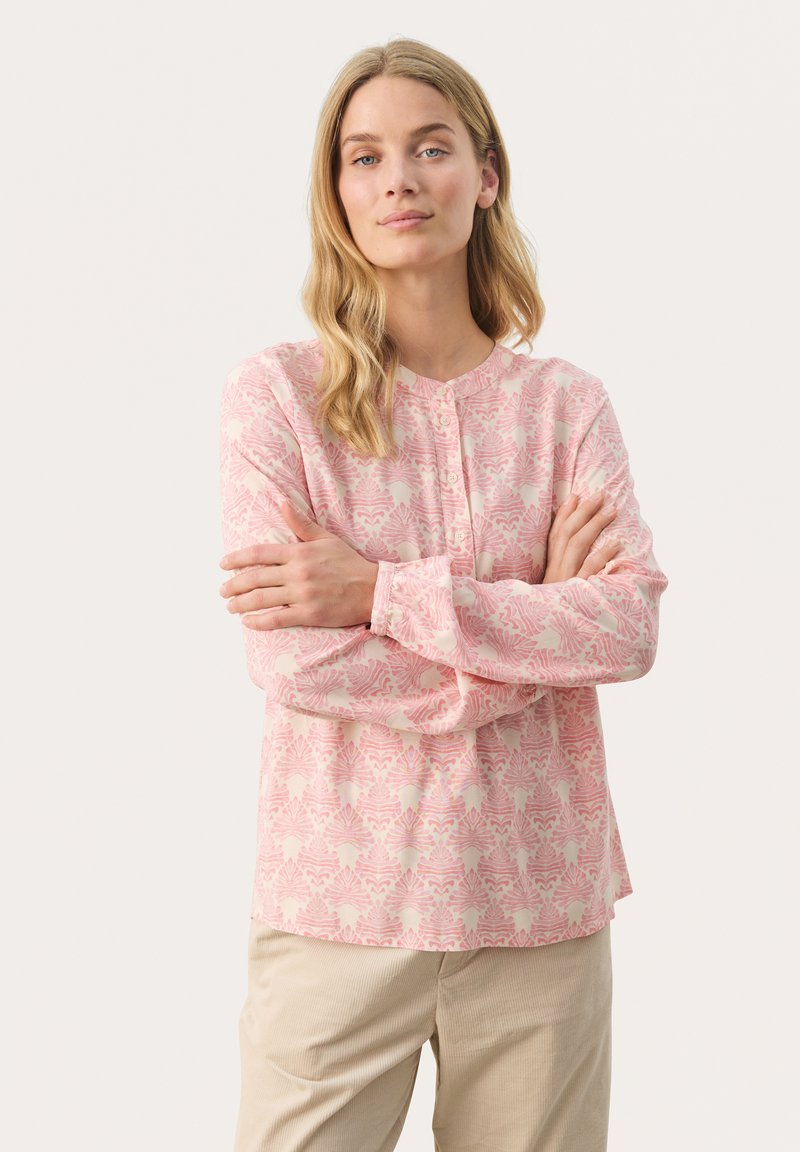 Langærmet, lyserød bluse med blomstermønster, blødt stof, rund halsudskæring og knaplukning foran. Parret med lysebeige bukser.