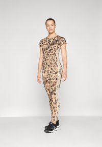 Leopardmønster aktivt tøy-sett i beige med korte ermer og slim-fit bukser med side-striper. Mønstret stoff med jevn tekstur.