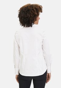 Weißes Langarmhemd mit tailliertem Design, geknöpften Manschetten und abgerundetem Saum. Glattes Baumwollmaterial mit einem klaren, minimalistischen Stil.