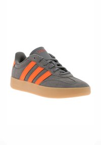 Gray suede sneaker with three bold orange stripes, rubber gum sole, and gray laces. Features a cushioned, rounded collar for comfort.