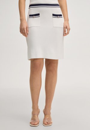 Witte knielange rok met een marineblauwe gestreepte tailleband en voorzakken met knoopdetails, gedragen met doorzichtige sandalen met hoge hak.