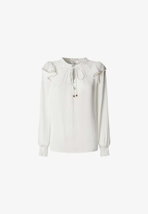 Balta blūze ar apaļu kakla izgriezumu, ar saites detaļu, pūkainām piedurknēm un dekoratīvo izšuvumu gar pleciem un aprocēm. Gluda auduma tekstūra.