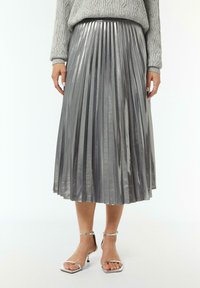 Zilveren geplooide midi-jurk met een glanzende textuur en een elastische tailleband, gecombineerd met metallic zilveren hakken sandalen.