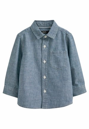 Child wearing a light blue button-up shirt and dark corduroy pants with hands clasped in front.