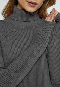 Gray ribbed turtleneck sweater made from soft fabric. Features a high collar, long sleeves, and textured pattern throughout.