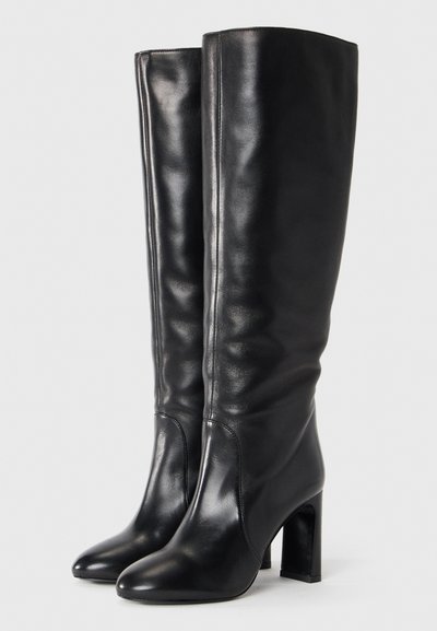Pair of tall black leather boots with pointed toes and block heels on a plain light background.