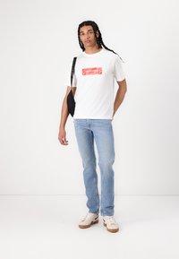 Hvid bomuld t-shirt med rødt logo print, parret med lyseblå jeans og off-white sneakers med brun sål. Sort crossover taske.