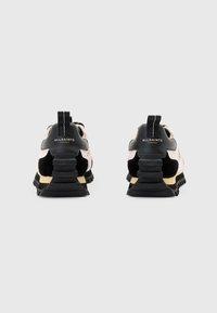 Schwarz-braune Sportschuhe mit einer Kombination aus glatten und strukturierten Materialien, ausgestattet mit einer erhöhten Ferse, einem Zugband und einer Markenkennzeichnung auf der Rückseite.