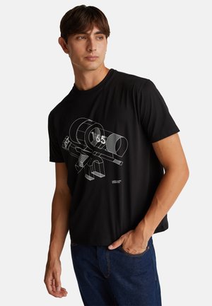 Camiseta de algodón negra con un diseño gráfico blanco de un arma con formas geométricas. Manga corta y cuello redondo. Combinada con unos vaqueros.