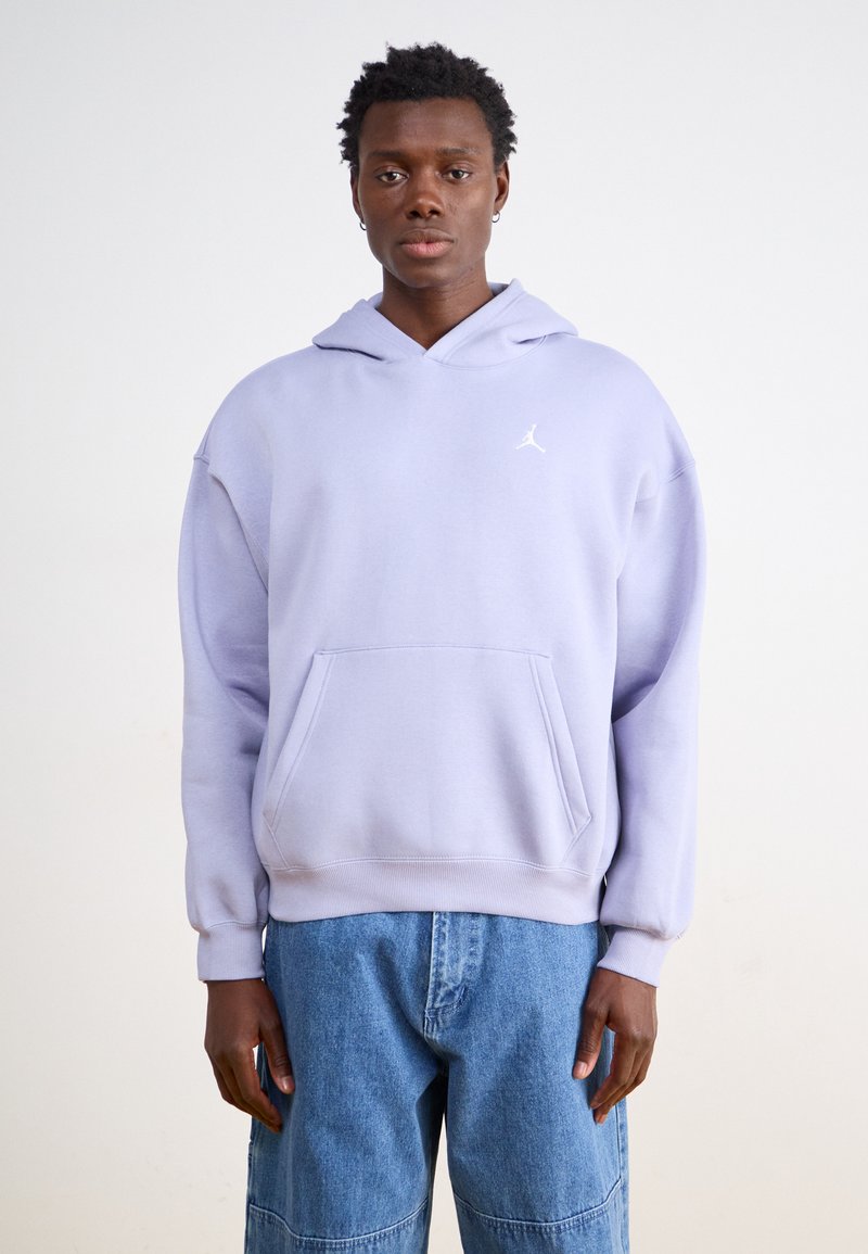 Felpa con cappuccio di un leggero colore viola, dotata di tasca frontale e logo bianco. Materiale morbido con polsini a coste. Indossata con pantaloni in denim blu.