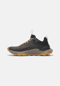 Zapato de senderismo para hombre en negro y gris, con parte superior de malla, suela resistente y cordones marrón claro. Incluye una pestaña en el talón.