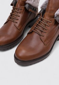 Botas de cuero marrón con una textura lisa, puntera redondeada, cordones en la parte delantera, forro de piel de fur en la parte superior y suela de goma resistente para una mejor tracción.