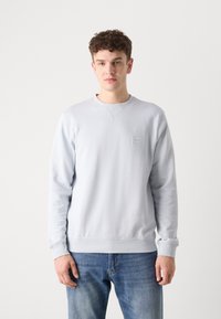 Sudadera de color azul claro, hecha de un tejido suave, con mangas largas, puños y dobladillo acanalados, y un pequeño parche de logo en el pecho.