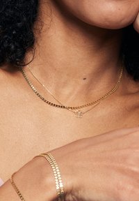 Złote naszyjniki warstwowe z płaskim łańcuchem i delikatnym wisiorkiem w kształcie kwiatu; bransoletki z połączonym złotym wzorem, wyróżniające się wypolerowanym wykończeniem.