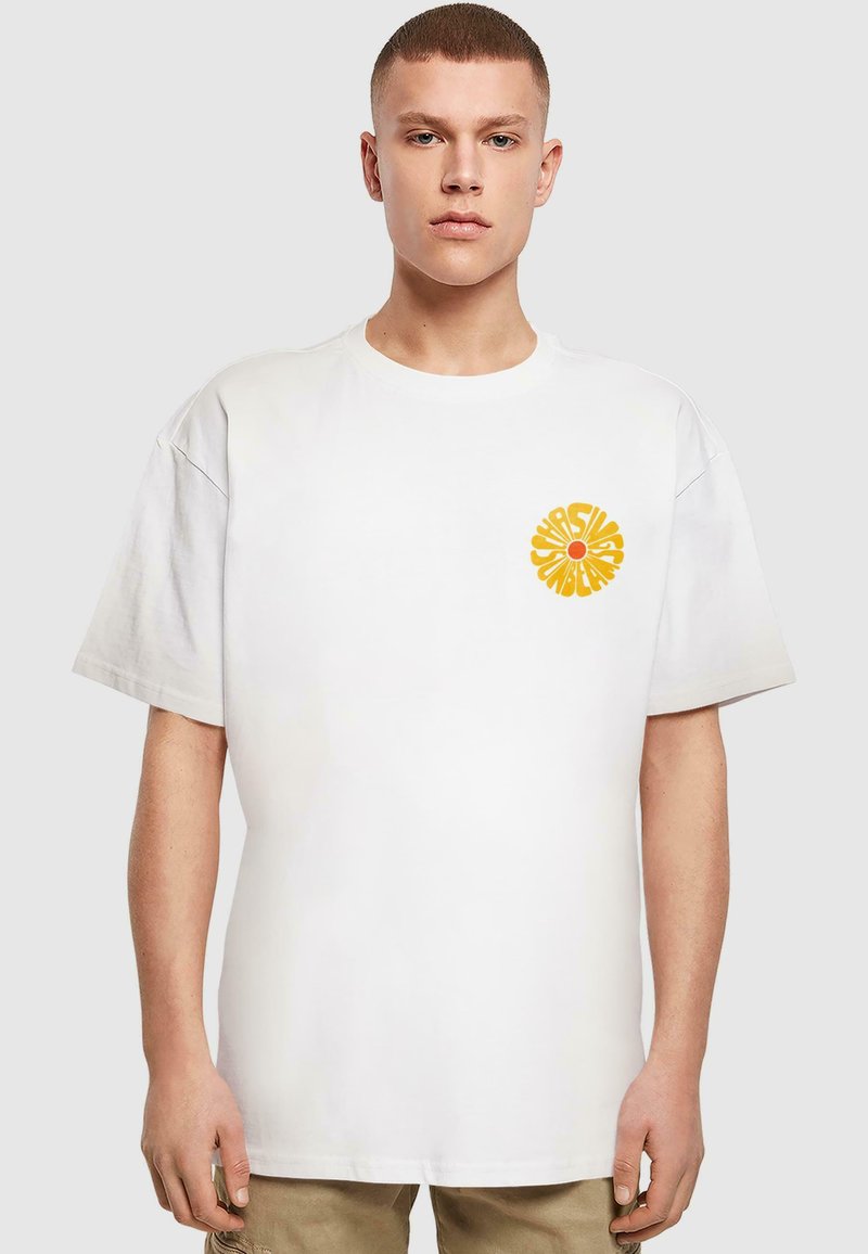 Hvid bomulds-t-shirt med korte ærmer og en afslappet pasform. Har et klart gult rundt grafisk motiv på venstre brystområde.