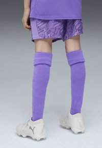 Completo da calcio viola composto da una maglia a maniche corte e pantaloni corti con fantasia. Il giocatore indossa calze viola fino al ginocchio e scarpini da calcio bianchi.