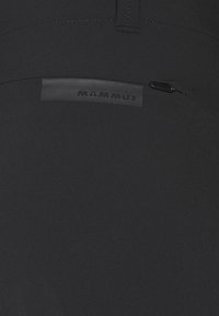 Svart tyg med en liten horisontell dragkedjeficka med en svart gummilapp med texten "MAMMUT."