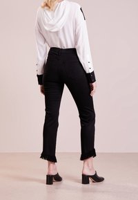 Jeans de mezclilla negros con dobladillo de flecos, combinados con una camisa blanca con capucha y mangas negras en contraste. Mule de tacón negro.