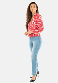 Blusa de manga larga con estampado rojo y rosa combinada con jeans rectos de tiro claro y zapatos de tacón negro. Tela suave y corte ajustado.